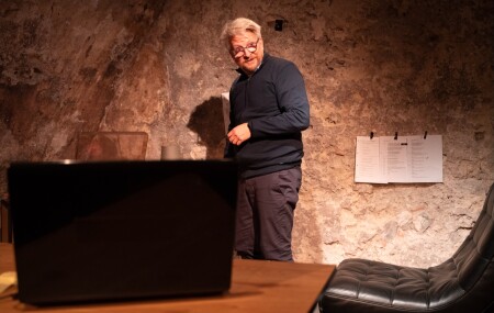 Der Schauspieler Sebastian Krähenbühl steht hinter seinem Computer. Er ist um die 50 Jahre alt und hat helles Haar und eine B