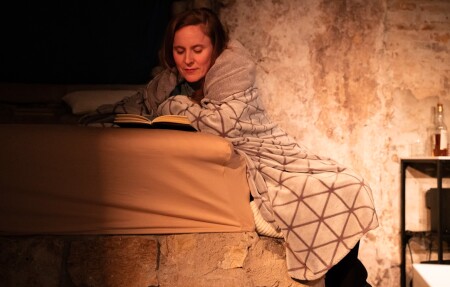 Die Schauspielerin Anna-Katharina Müller liest in einem Buch. Sie ist in eine Decke eingehüllt. Sie ist Mitte vierzig und ha