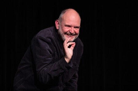 Der Schauspieler in einer Nahzaufnahme ohne Bischofsgewand. Er lächelt böse, wie der Teufel.