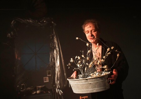 Die Dragqueen hät einen Zuber in der Hand. Er ist gefüllt mit getrockneten Blumen.