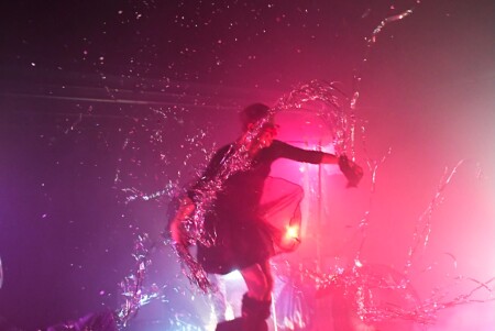 Die Lichtstimmung ist rosa. Die Dragqueen tanzt im Licht und im Nebel.